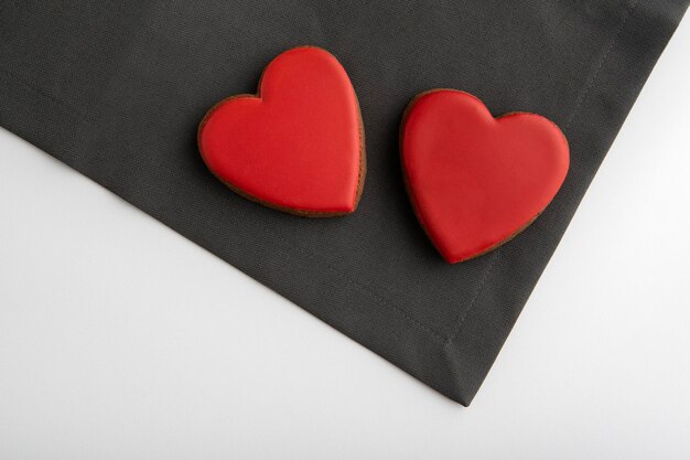 Dois biscoitos vermelhos em forma de coração com glacê de açúcar. Fundo cinza e branco. Dia dos namorados.