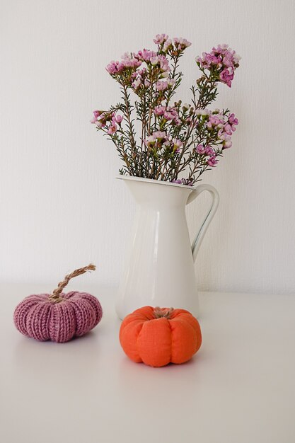 Foto dois brinquedos de malha roxa e laranja em miniatura de abóbora e um frasco branco com flores em branco