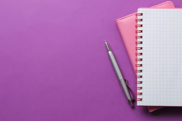 Foto dois caderno e uma caneta sobre um fundo roxo brilhante. vista do topo. ferramentas de escritório. espaço para texto