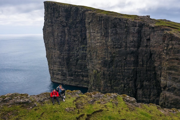 Dois caminhantes sentados à beira de um penhasco nas ilhas faroe