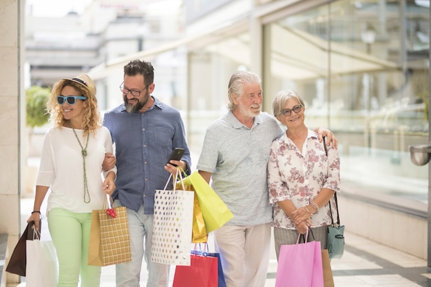 Dois casais de dois adultos e dois idosos vão às compras juntos no shopping com muitas sacolas com roupas e muito mais nas mãos - quatro pessoas felizes curtindo