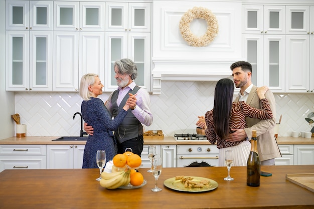 Dois casais, pais e jovem marido e mulher dançando na cozinha leve e elegante em casa, festa