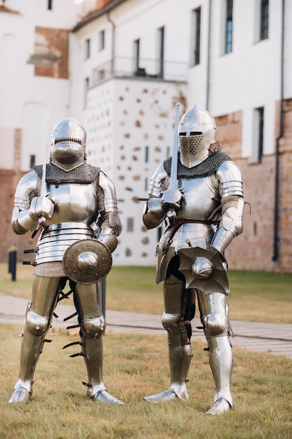 Dois cavaleiros em armaduras de metal antigas ficam na parede de pedra do castelo