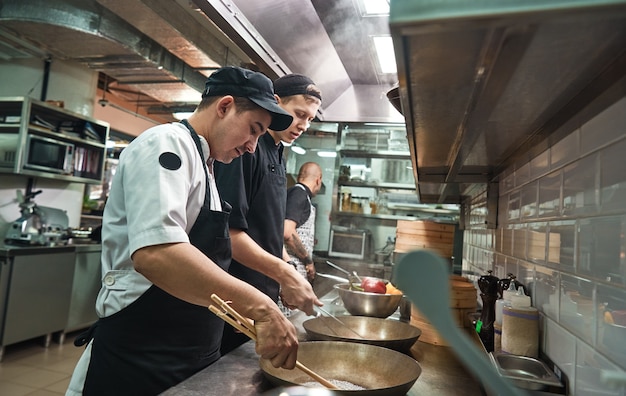 dois chefs assistentes cozinhando um novo prato na cozinha de um restaurante