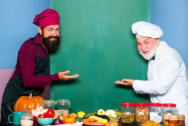 Dois chefs com chapéu de cozinheiro apontando colher no menu do quadro em branco Chef de cozinha