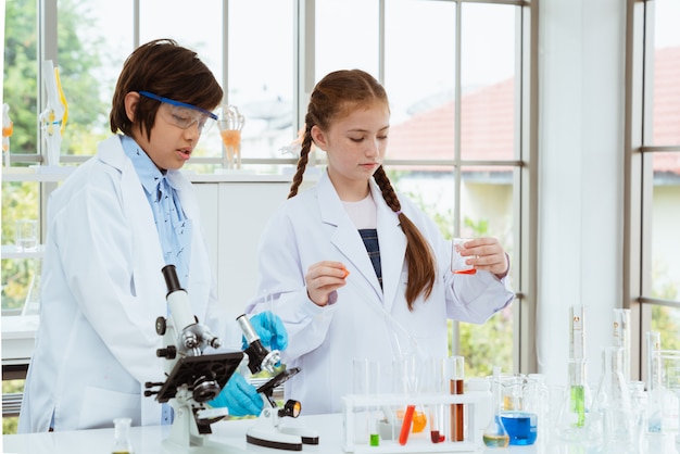 Dois cientistas das crianças que fazem experiências químicas com vista do microscópio na sala do laboratório.