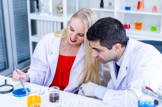 Dois cientistas estão trabalhando olhando para o tubo de ensaio com amostra em um cientista de laboratório de química ou jovem pesquisador feminino e masculino está fazendo investigações em fundo de análise de laboratório