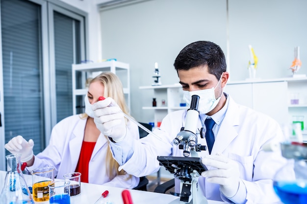 Dois cientistas estão trabalhando segurando olhando para tubo de ensaio com amostra em um cientista de laboratório de química ou jovem pesquisador feminino e masculino estão fazendo investigações em fundo de análise de laboratório