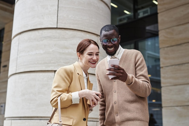 Dois colegas alegres em roupas de luxo quietas olhando para a tela do smartphone