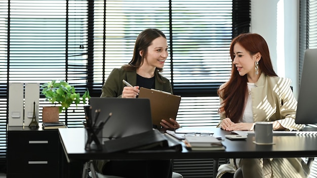 Dois colegas de trabalho sorridentes discutindo sobre um novo projeto de negócios e planejando uma estratégia de marketing no escritório moderno