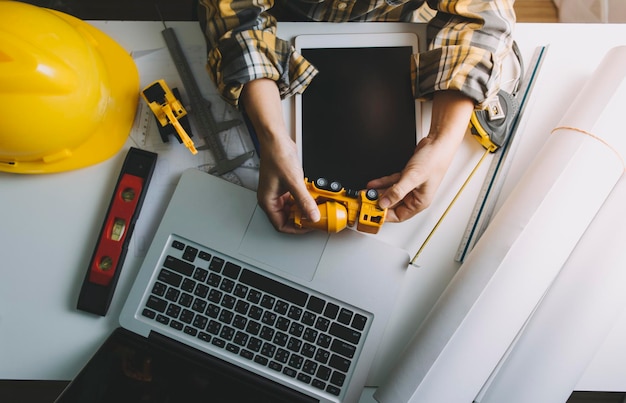 Dois colegas discutindo trabalho de dados e tablet laptop com projeto arquitetônico no canteiro de obras na mesa no escritório