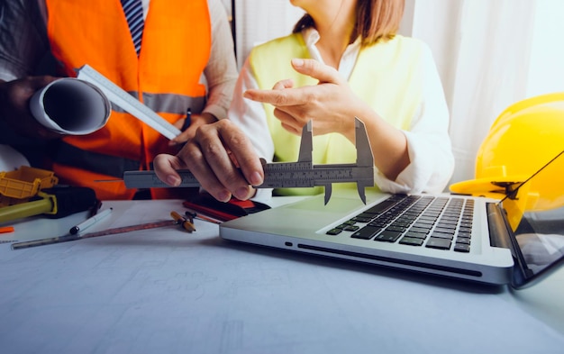 Dois colegas discutindo trabalho de dados e tablet laptop com projeto arquitetônico no canteiro de obras na mesa no escritório