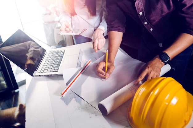 Dois colegas discutindo trabalho de dados e tablet laptop com projeto arquitetônico no canteiro de obras na mesa no escritório