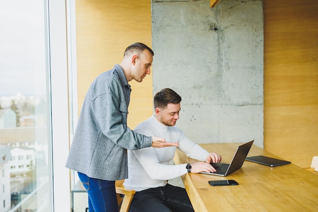 Dois colegas do sexo masculino enquanto trabalham com um laptop no escritório Dois empresários orientados a objetivos colaboram em um espaço de trabalho moderno Dois jovens empresários trabalham em um escritório bem iluminado