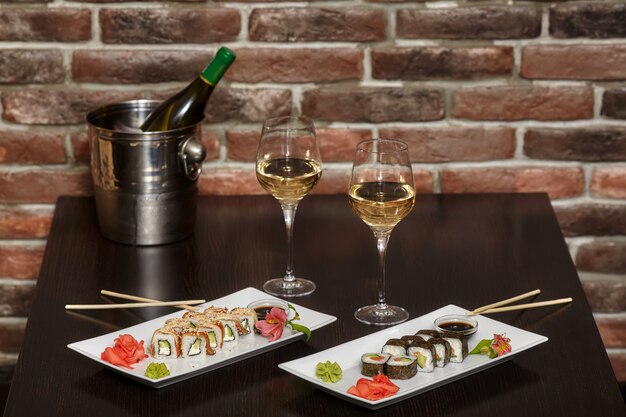 Dois conjuntos de sushi rola na chapa branca com pauzinhos e copos de vinho