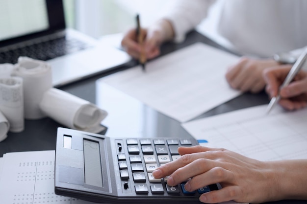 Dois contadores usam uma calculadora e um laptop para contar impostos ou saldo de receitas. Conceitos de negócios, auditoria e impostos