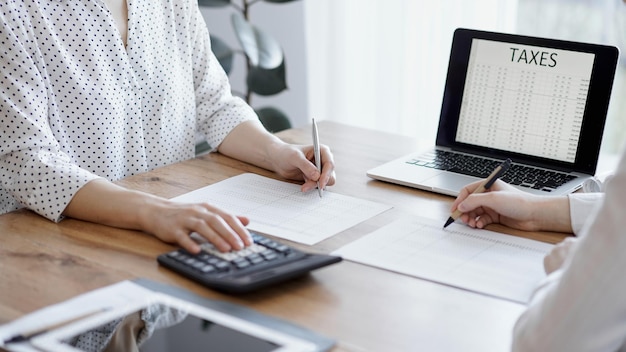 Dois contadores usando um laptop e uma calculadora enquanto contam impostos na mesa de madeira no escritório. Trabalho em equipe em auditoria de negócios e finanças