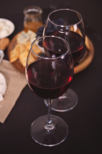 Dois copo de vinho tinto e prato com queijo variado, frutas e outros petiscos para festa