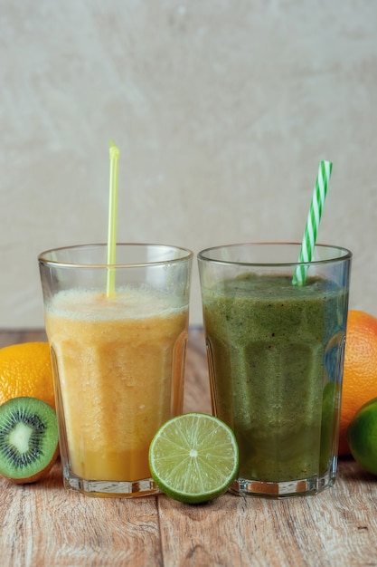 Dois copos altos com smoothies de kiwi e espinafre rodeados por frutas em uma mesa de madeira. O conceito de perder peso e nutrição adequada