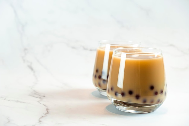 Dois copos com chá de bolha de leite com deliciosas pérolas de tapioca em fundo de mármore famoso chá de geléia de leite de taiwan bebidas da moda com espaço de cópia