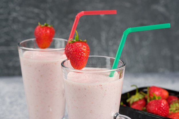 Dois copos com milk-shake de morango com pedaços de frutas na borda do copo.