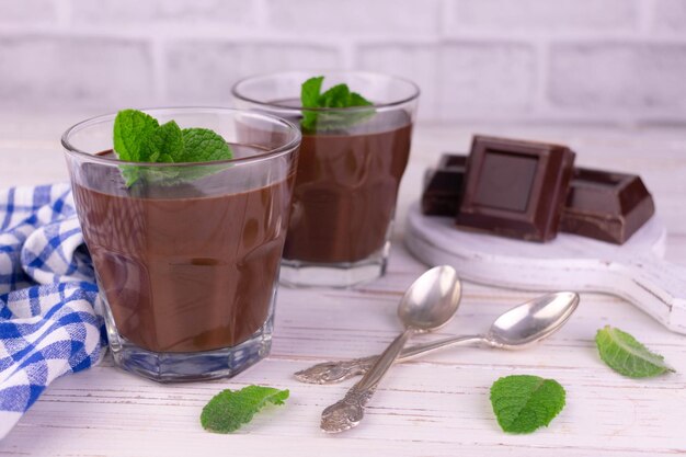 Dois copos com pudim de chocolate em um fundo branco de madeira