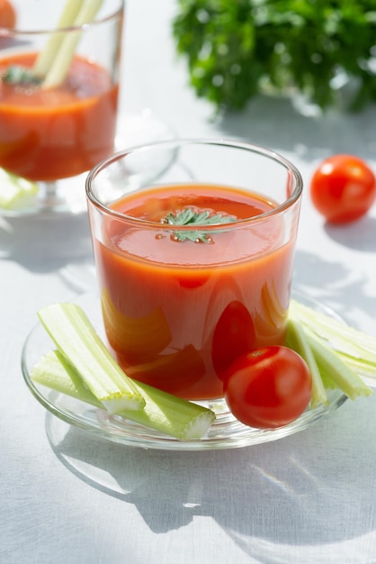 Dois copos com salsa de aipo de suco de tomate fresco e tomates maduros sobre fundo claro