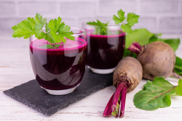 Dois copos com suco de beterraba saudável em um fundo branco de madeira.