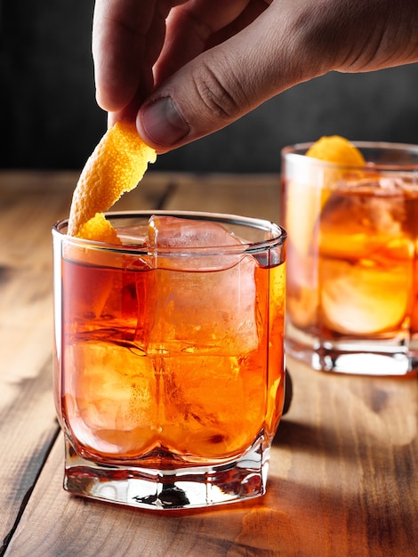 Dois copos com um coquetel Negroni em uma mesa de madeira. Foto vertical.