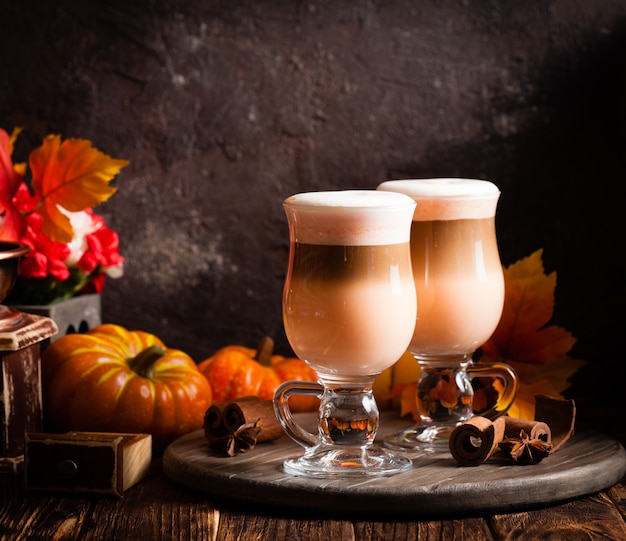 Dois copos de café com leite picante de abóbora com chantilly e canela em um suporte de madeira