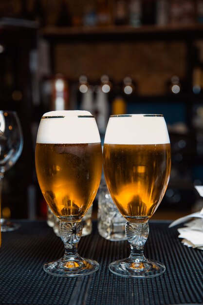 Dois copos de cerveja gelada espumosa em um balcão escuro de bar