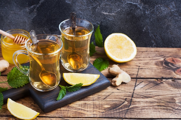 Dois copos de chá de ervas natural gengibre limão hortelã e mel em um fundo de madeira. Copie o espaço