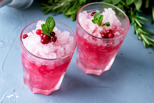 Dois copos de coquetel frio com cranberry e vodka decorado com menta e cranberries maduros fundo azul bebida de verão