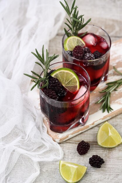 Dois copos de deliciosa limonada refrescante com amora, gelo e limão, decorado com alecrim.