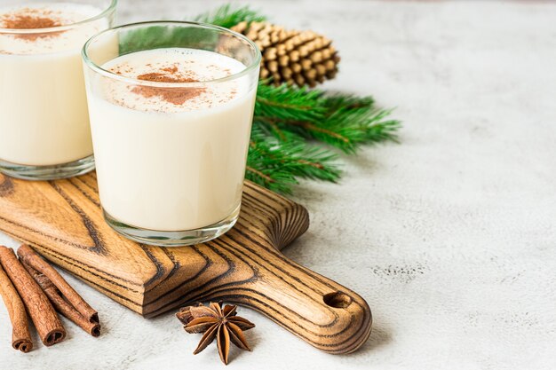 Dois copos de gemada e decorações de Natal em fundo cinza