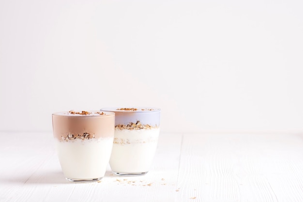 Dois copos de kefir caseiro com granola estão sobre uma mesa de madeira branca.