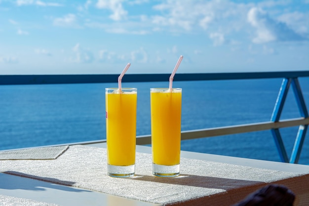 Dois copos de laranja sentados em uma mesa em um café à beira-mar em um resort à beira-mar