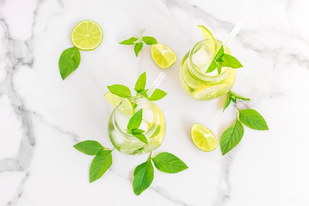 Dois copos de limonada ou coquetel de mojito com limão e hortelã, bebida refrescante gelada ou bebida com gelo no fundo de mármore branco.