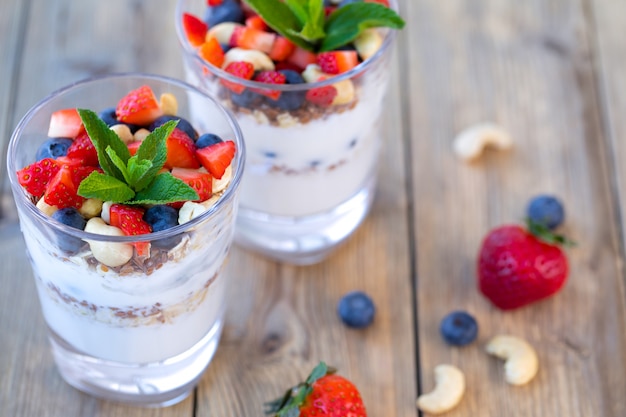 Dois copos de morango parfait feito de frutas frescas, iogurte, mirtilos, sementes de linho e muesli em um fundo de madeira.