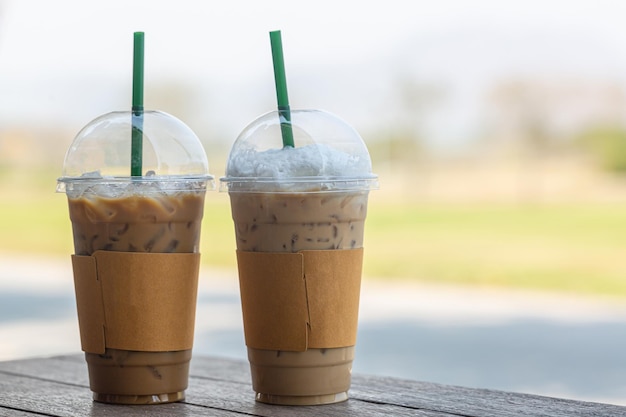 Dois copos de plástico com café preto gelado americano e café com leite gelado na mesa de madeira no caixão