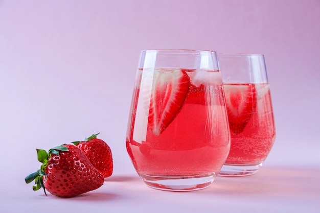 Dois copos de sangria de morango com espumante, morango e cubos de gelo em taça de champanhe