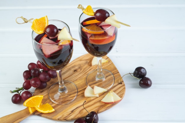 Dois copos de sangria sobre uma base de madeira branca. Bebida tradicional espanhola com decoração de frutas. Copie o espaço.