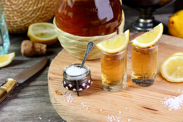 Foto dois copos de tequila com limão e sal em uma bandeja de madeira