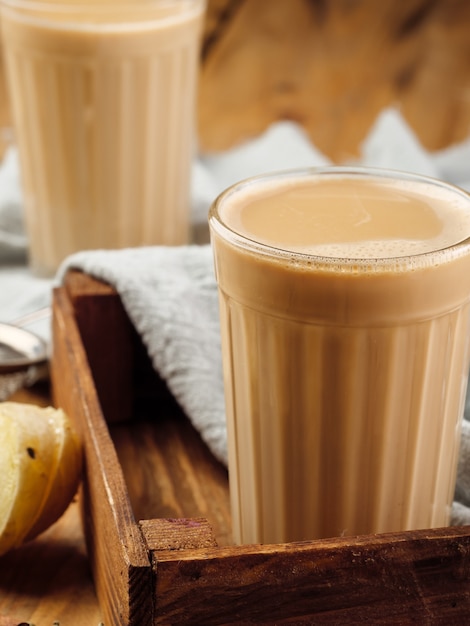 dois copos de vidro facetado sobre uma mesa de madeira com a tradicional bebida indiana masala chai.