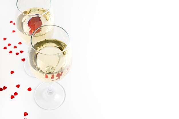 Dois copos de vinho branco e decoração de corações. Taças de vinho sobre um fundo branco com espaço de cópia.