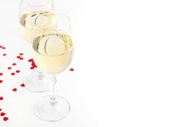 Dois copos de vinho branco e decoração de corações. Taças de vinho sobre um fundo branco com espaço de cópia.