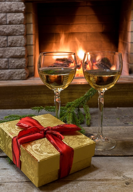 Dois copos de vinho branco, presente de Natal em uma caixa perto de firepace aconchegante.