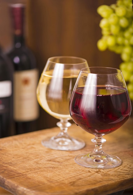 Dois copos de vinho com vinho branco e tinto e uvas em fundo de madeira.