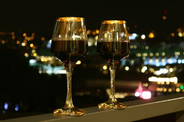 Dois copos de vinho na varanda com visão noturna da cidade embaçada ao fundo