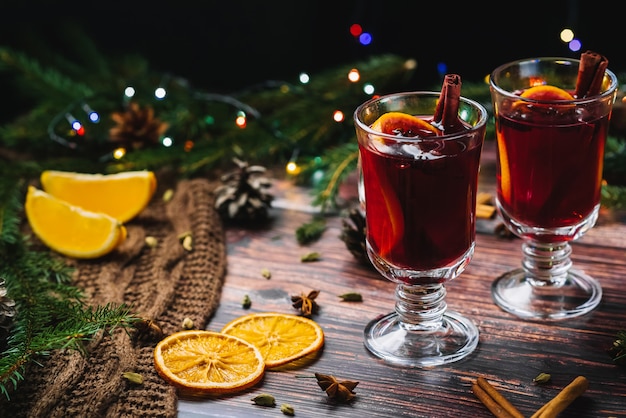 Dois copos de vinho quente com especiarias e fatias de laranja em uma mesa rústica de madeira